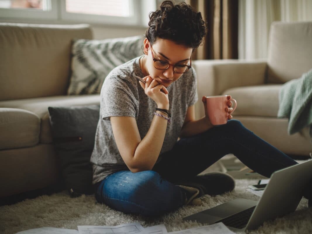En kvinna sitter i soffan med en laptop i knät och arbetar fokuserat i hemmamiljö.