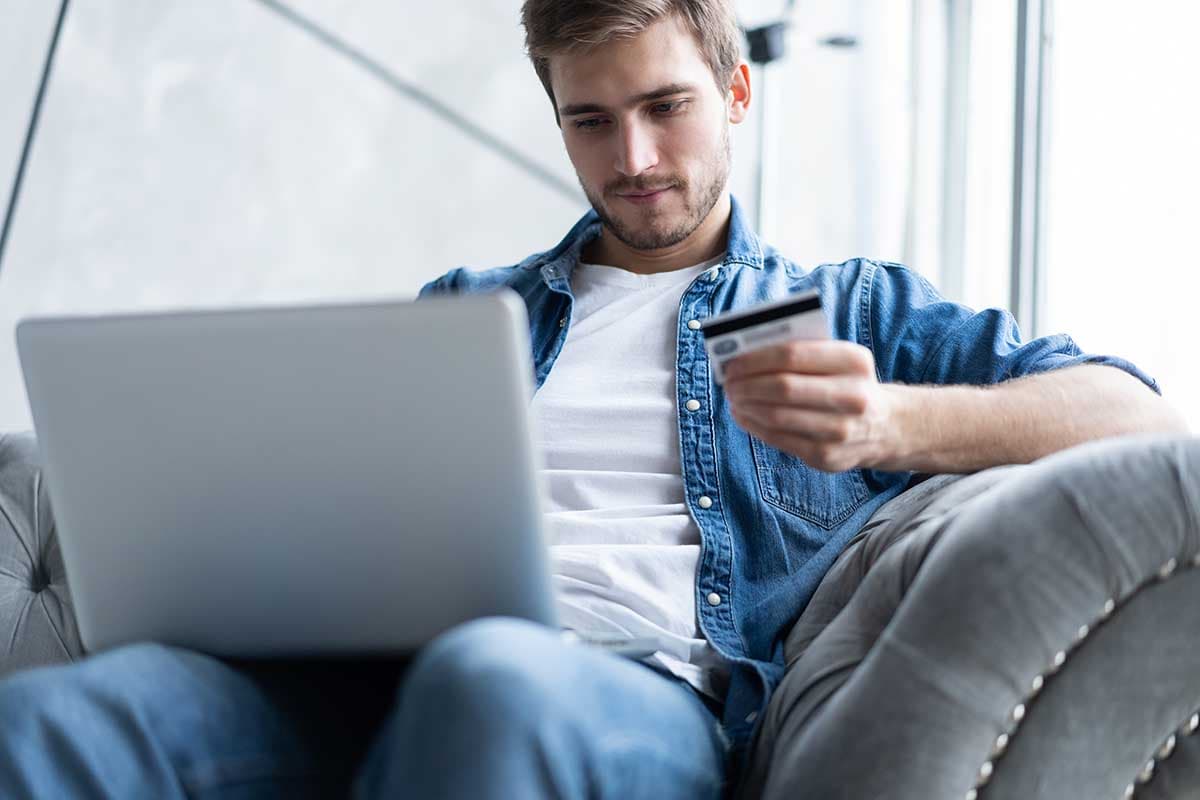 En man sitter på soffan med en bärbar dator i knät och ser fundersam ut.