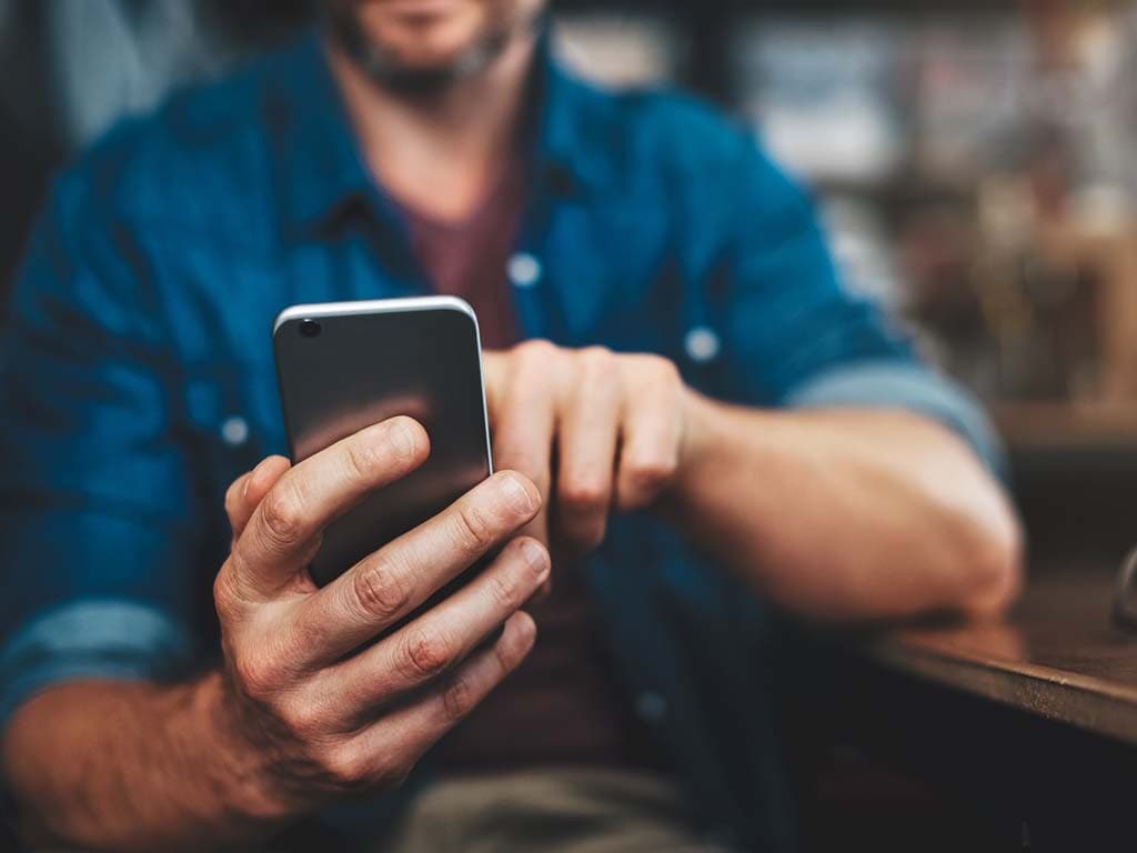 Närbild på en man som använder sin smartphone med båda händerna.