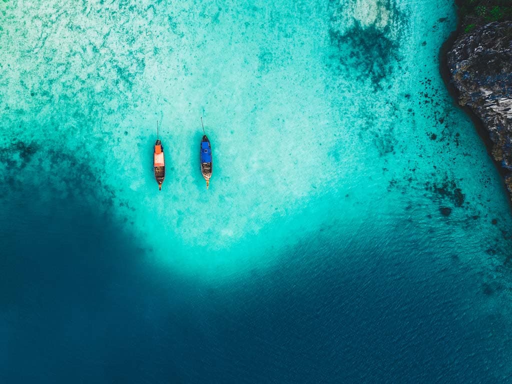 Flygbild över turkost tropiskt vatten med två båtar som flyter ovanför korallrev.