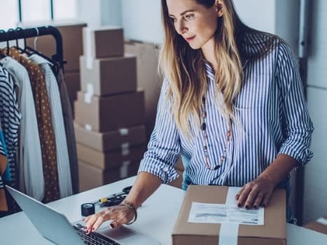 En kvinna arbetar hemifrån vid ett bord med laptop, anteckningsbok och kaffe.
