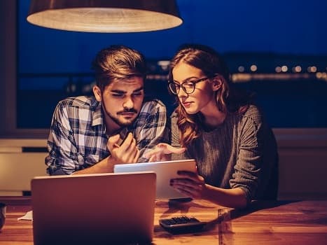 Ett par sitter vid ett bord med laptop och dokument, ser oroliga ut.