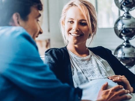 En gravid kvinna pratar med en läkare eller barnmorska i ett vårdrum.