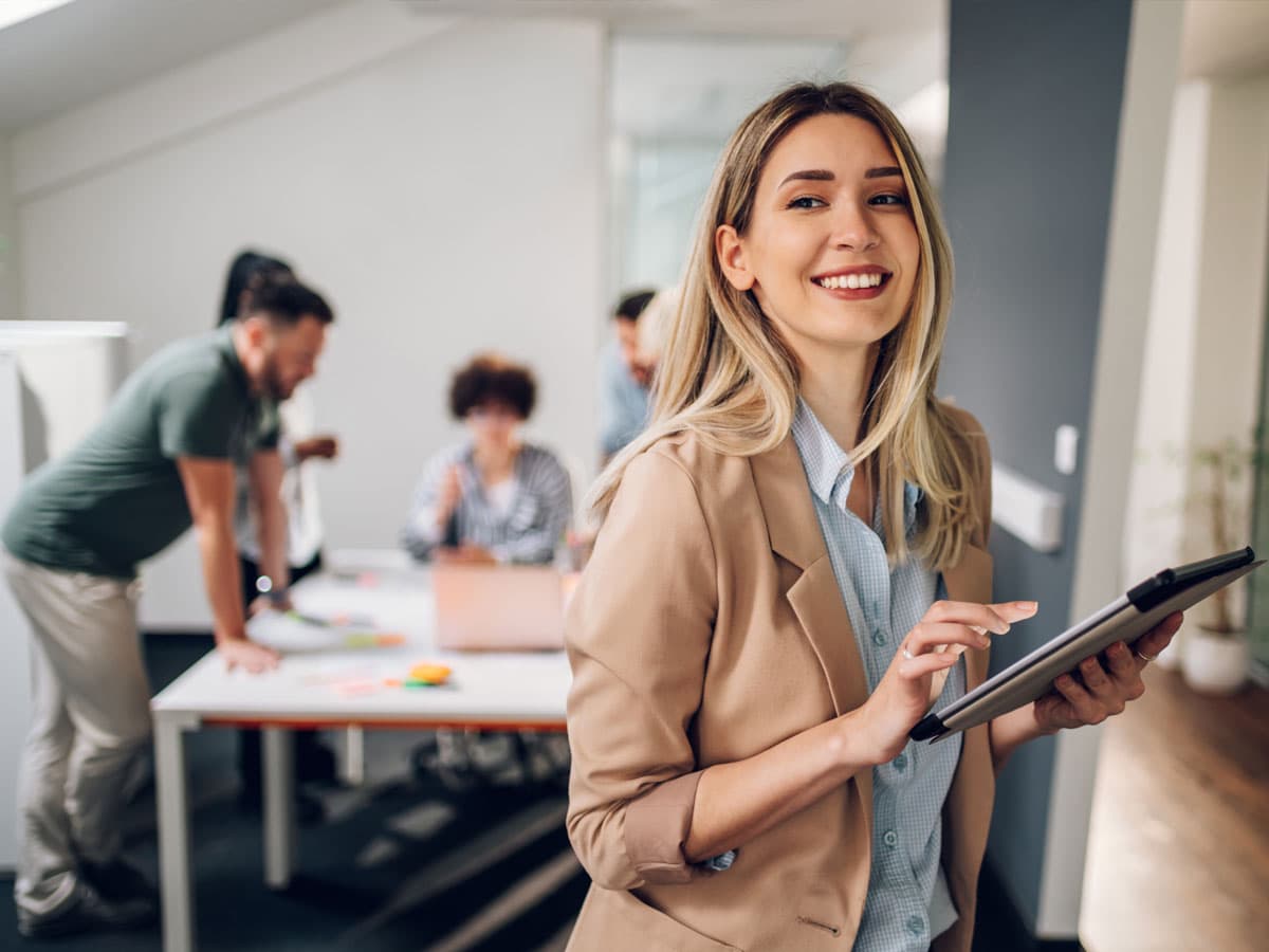 En kvinna står i ett ljust kök och tittar ner på sin mobiltelefon med ett leende.