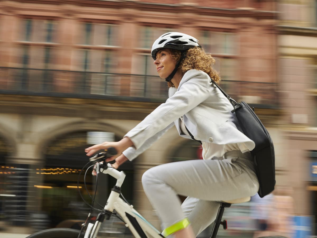En kvinna sitter i en ljus vardagsrumsmiljö med en laptop i knät och ler.
