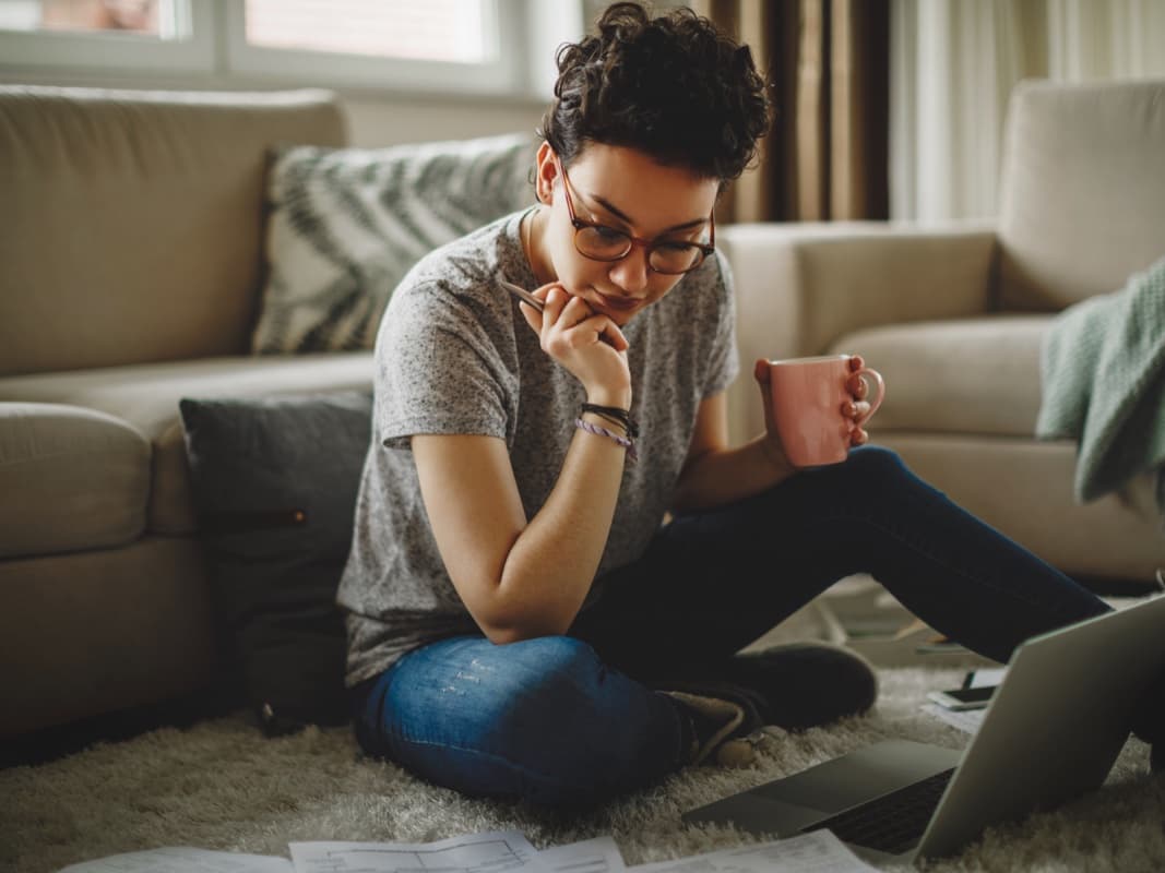 En kvinna sitter i soffan med en bärbar dator i knät, koncentrerad på sitt arbete.