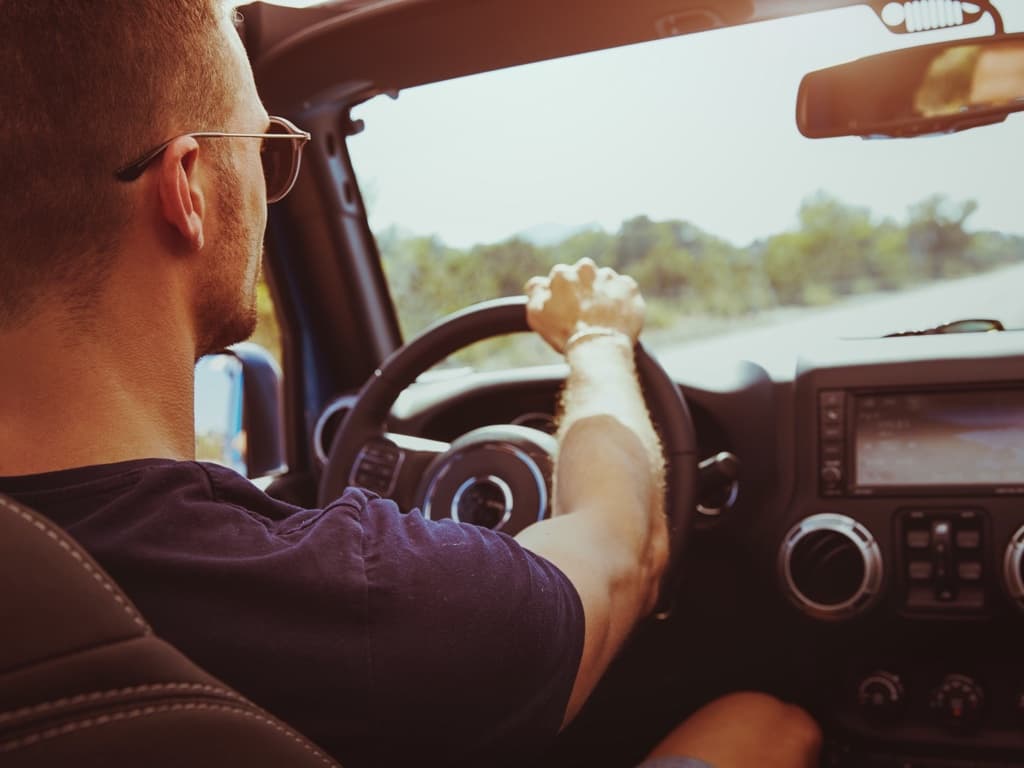 En man kör bil på en landsväg, fotograferad inifrån fordonet.