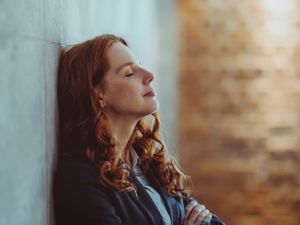 En kvinna lutar huvudet mot en vägg med slutna ögon, ser avslappnad och lättad ut.